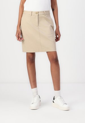Khakifarbener Baumwoll-Bleistiftrock mit glatter Textur, vorderer Knopfverschluss und dezenten Seitentaschen, kombiniert mit weißen Sneakers und Socken.