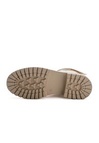 Semelle en caoutchouc beige clair avec des rainures profondes et une surface texturée. Le talon présente une légère courbure ; il arbore une couleur lisse et neutre.