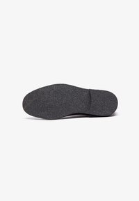 Talpa unei încălțări, cu un material din cauciuc texturat de culoare neagră. Forma este ovală, cu o ușoară îngustare spre partea de vârf.