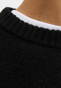 Czarny sweter dzianinowy z ribbowanym dekoltem, z kontrastującym białym wewnętrznym kołnierzykiem. Tekstura wydaje się miękka i nieco puszysta.