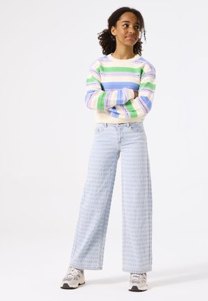 Pull rayé multicolore dans des teintes pastel ; jean léger bleu clair à jambe large avec un motif subtil ; baskets grises avec des accents noirs.