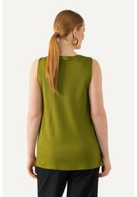 Top verde senza maniche con una texture liscia, un collo rotondo e una vestibilità rilassata, abbinato a pantaloni neri.