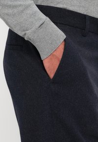 Navy wool trousers with a soft texture and a side pocket, paired with a light grey knitted sweater showcasing ribbed cuffs.