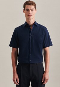Camicia button-up a maniche corte, blu navy, con taschino sul petto; tessuto liscio, design con colletto, dotata di bottoni scuri e una vestibilità sartoriale.