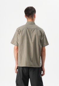 A person with short hair wearing a short-sleeve beige and navy checkered shirt, facing away against a plain white background.