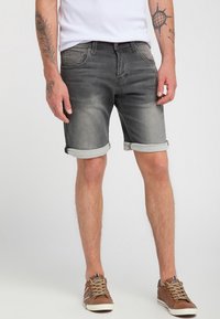 Shorts en denim gris avec des poignets retroussés, dotés d'un design classique à cinq poches et d'un léger dégradé. Portés avec un t-shirt blanc et des baskets marron.