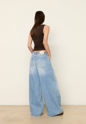 Jean en denim bleu clair à jambes larges avec un délavage, taille élastique, associé à un débardeur marron ajusté.