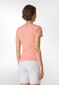 Ferskenfarvet tætsiddende t-shirt med korte ærmer og rund halsudskæring. Har et lille lyserødt mærke bagpå. Bæres over hvide shorts.
