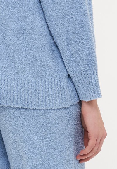 Light blue, textured sweater with ribbed hem and sleeves. Soft, fluffy fabric. Close-up showing sleeve and wrist detail.