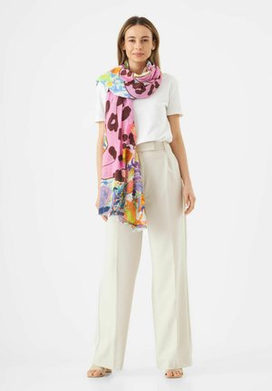 Écharpe légère à motif fleuri en rose, avec des accents orange, vert et bleu, drapée sur un haut blanc, portée avec un pantalon beige.