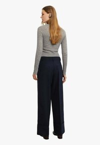 Maglione grigio a coste, pantaloni ampi blu navy con risvolti piegati e scarpe nere. Vista posteriore che mostra i dettagli delle cuciture e la texture del tessuto.