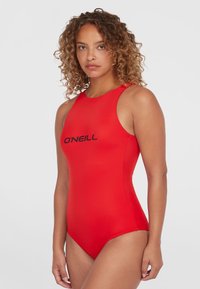 Rød badedragt i én del med høj halsudskæring, tynde stropper og sort "O’Neill" logo. Glat, strækbart materiale med en slank, tætsiddende silhuet.