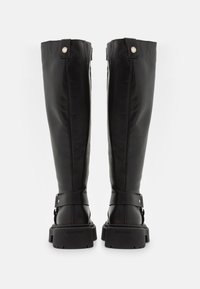 Botas altas de cuero negro con una textura lisa, que cuentan con un tubo ancho, correa en el tobillo, detalles en plata y suela gruesa y con tracción.