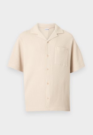 Chemise beige en maille à manches courtes avec col camp, boutons sur le devant et poche poitrine, présentée sur un fond uni.