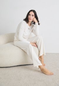 Ensemble de vêtements de détente couleur crème comprenant un haut à manches longues avec un col rond et un pantalon ample, tous deux en textile doux.