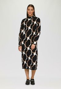 Langsleeve, aansluitende jurk in zwart en wit met een geometrisch patroon van golvende vormen omlijnd in beige. Hoge halslijn, knie-lengte.