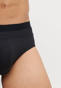 Melni apakšveļa ar gludu tekstūru un elastīgu jostasvietu, kuras dizainā ir subtīls logos. Dizains nodrošina pilnīgu segumu un ciešu piegulšanu.