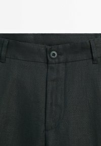 Dark linen pants featuring a straight cut, button closure at the waist, and subtle texture. Includes side pockets and clean, tailored lines.