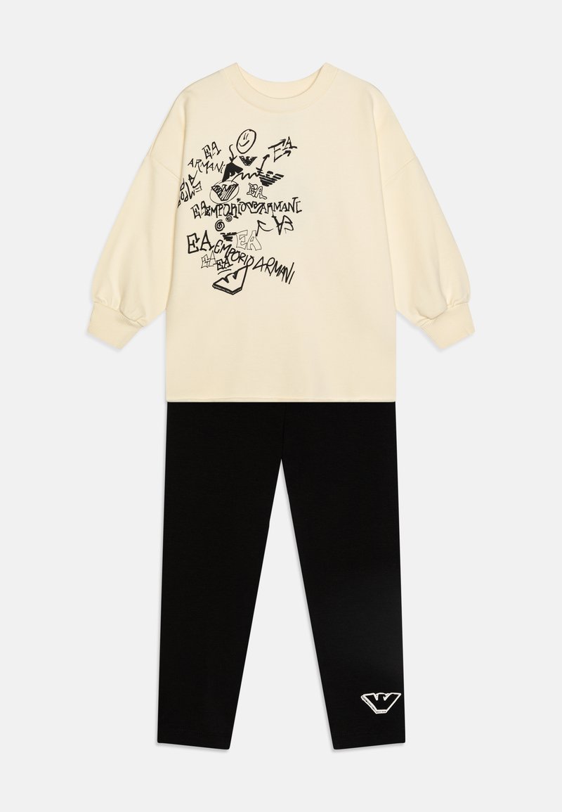 Felpa crema con stampe grafiche nere, maniche lunghe, abbinata a leggings neri con un logo bianco sulla caviglia. Tessuto morbido.