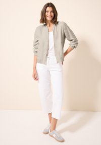 Giubbotto bomber grigio chiaro, t-shirt bianca, pantaloni cropped bianchi e sneaker grigie con lacci bianchi. Design semplice, look casual, dettagli privi di cucitura.