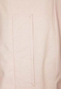 Ljusrosa tyg med en slät textur som har en rektangulär lapplomme och kontrasterande sömnadsdetaljer.