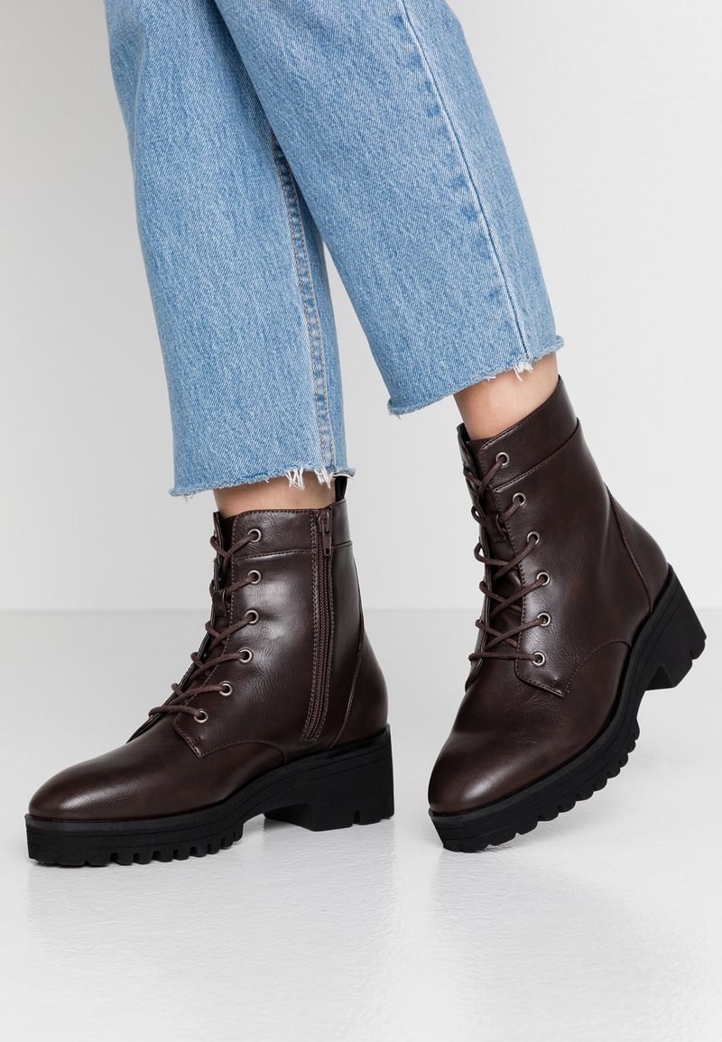 Bottes basses en cuir marron avec une finition texturée, bout rond, design à lacets, détail avec fermeture éclair et semelle extérieure en caoutchouc noire épaisse.