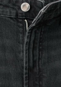 Črne kavbojke iz jeansa z zadrgo in srebrnim gumbom. Imajo teksturirano tkanino in tonirano šivanje za enoten videz.