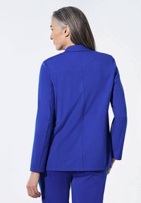 Veste bleue ajustée avec manches longues, en tissu lisse et coupe droite. Présente un col cranté et des détails de couture minimalistes.
