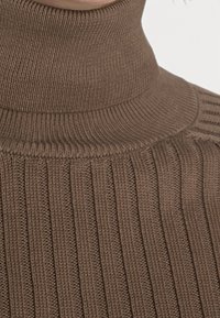Brauner gerippter Rollkragenpullover mit hohem Kragen, strukturiertem Strickdesign und vertikalen Linien für zusätzlichen visuellen Reiz.