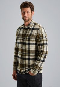 Geruite shirt met olijfgroene, beige en marineblauwe patronen. Gemaakt van textuurstof met een knoopsluiting aan de voorkant en een patch op de linker schouder.