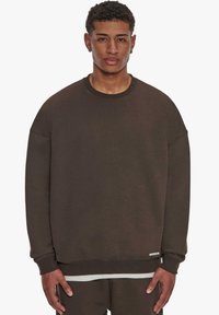 Dunkelbrauner Sweatshirt mit Rundhalsausschnitt, überschnittenen Schultern, gerippten Bündchen und weicher Textur. Verfügt über ein kleines Etikett am Saum.