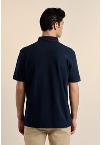 Polo de color navy con un patrón liso, de manga corta y cuello con un sutil ribete rojo, confeccionado en una tela suave.