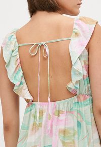 Πίσω όψη ενός ελαφρού, λουλουδάτου φορέματος με χρώματα μέντας, ροζ και μπεζ. Διαθέτει ρυτιδιασμένους ιμάντες και κλείσιμο με κόμπο στο πίσω μέρος.