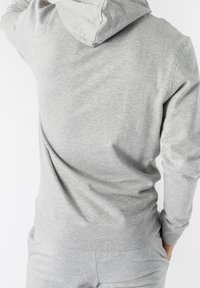 Grå huvtröja gjord av mjukt bomullsmaterial. Har en kenguruficka, ribbade muddar och en huva med snörning. Enkel design med minimala detaljer.