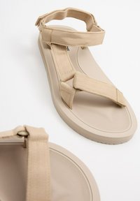 Sandalias beige con suela plana, correas de nylon ajustables y una base texturizada. Presenta un diseño minimalista y costuras reforzadas.