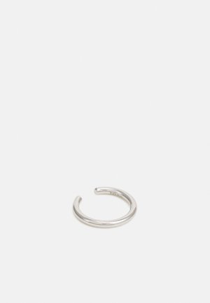 Bague minimaliste ouverte de ton argent avec une finition lisse, présentée sur un fond gris clair uni.