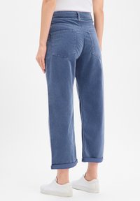 Jean en denim bleu à coupe décontractée, avec une taille haute, des revers roulés et deux poches arrière. Porté avec des baskets blanches.