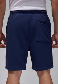 Marineblå bomulds shorts med elastisk talje, med en baglomme og en syet kant ved benene. Blød tekstur og afslappet design.