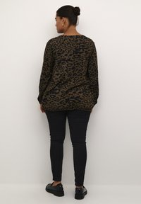 Leopardenmuster-Shirt in Braun und Schwarz, mit langen Ärmeln und rundem Ausschnitt, kombiniert mit schwarzen Skinny-Jeans und schwarzen Schuhen.