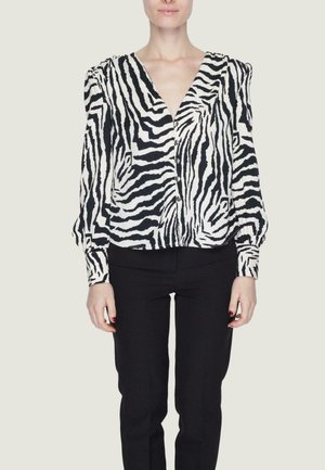 Blusa a strisce zebra bianca e nera con scollo a V profondo, maniche lunghe, chiusure a bottone e vestibilità comoda. Abbinata a pantaloni neri.