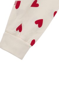 Crème kleurige stof met rode hartpatronen, featuring een strak manchet aan de onderkant. Zachte textuur en elastische band voor een veilige fit.