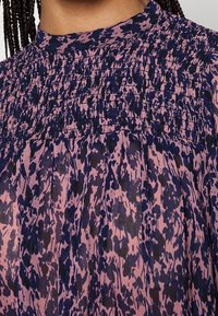 Blomstermønstret bluse i pink og marineblå, med en høj smocket halsudskæring og løs, samlet tekstur i stoffet.