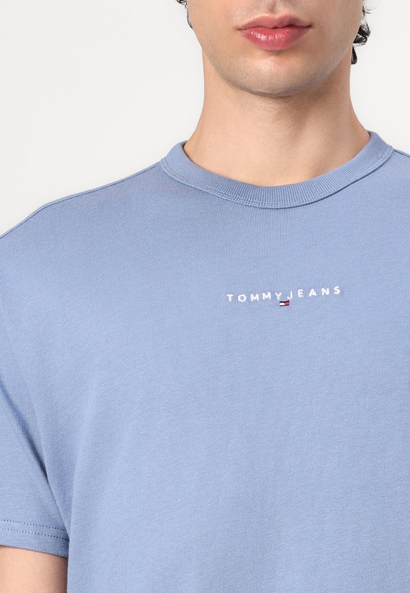 T-shirt en coton bleu clair avec un col rond, affichant le logo "TOMMY JEANS" brodé sur la poitrine. Manches courtes, tissu texturé.