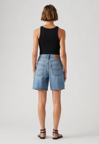 Shorts de mezclilla azul con un ajuste relajado, dobladillo deshilachado y dos bolsillos traseros. Se llevan con una camiseta negra sin mangas y sandalias oscuras.