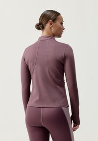 Langærmet atletisk top i mauve med høj krave, tætsiddende pasform og diskrete sømme. Blødt, strækbart stof fremmer bevægelse.