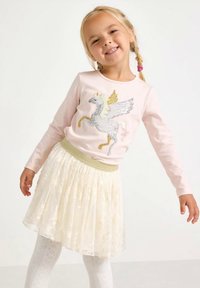 Hellrosa Langarmshirt mit einem glitzernden Einhorn-Motiv, kombiniert mit einem cremefarbenen, plissierten Rock, akzentuiert durch einen goldenen elastischen Bund.