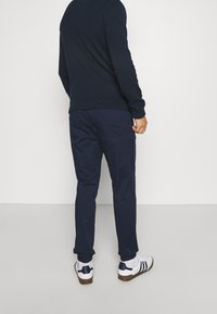 Marinblå stickad tröja och matchande byxor, med elastiska muddar och sidofickor. Vita sneakers med marinblå accenter på hälen.