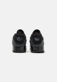 Black athletic shoes with a smooth texture and matte finish, featuring a patterned accent and a pull tab on the heel for easy wear.