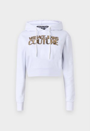 Balta siaurinta su kapuciu, turinti ryšių juostelę. Priekyje puikuojasi auksinės spalvos "VERSACE JEANS COUTURE" logotipas, o rankogaliai ir apatinė dalis yra tanksnti.