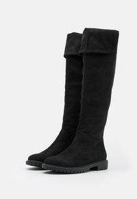 Botas de ante negras hasta la rodilla con un upper doblado, punta redondeada y suela de goma texturizada para mayor agarre. Acabado suave con acentos mínimos.